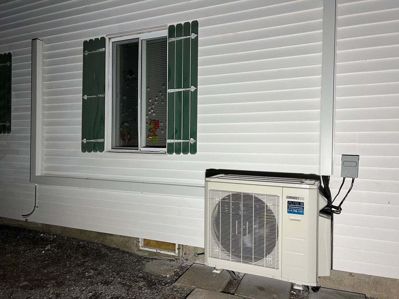 Une maison blanche avec des volets verts et un climatiseur blanc sur le côté.