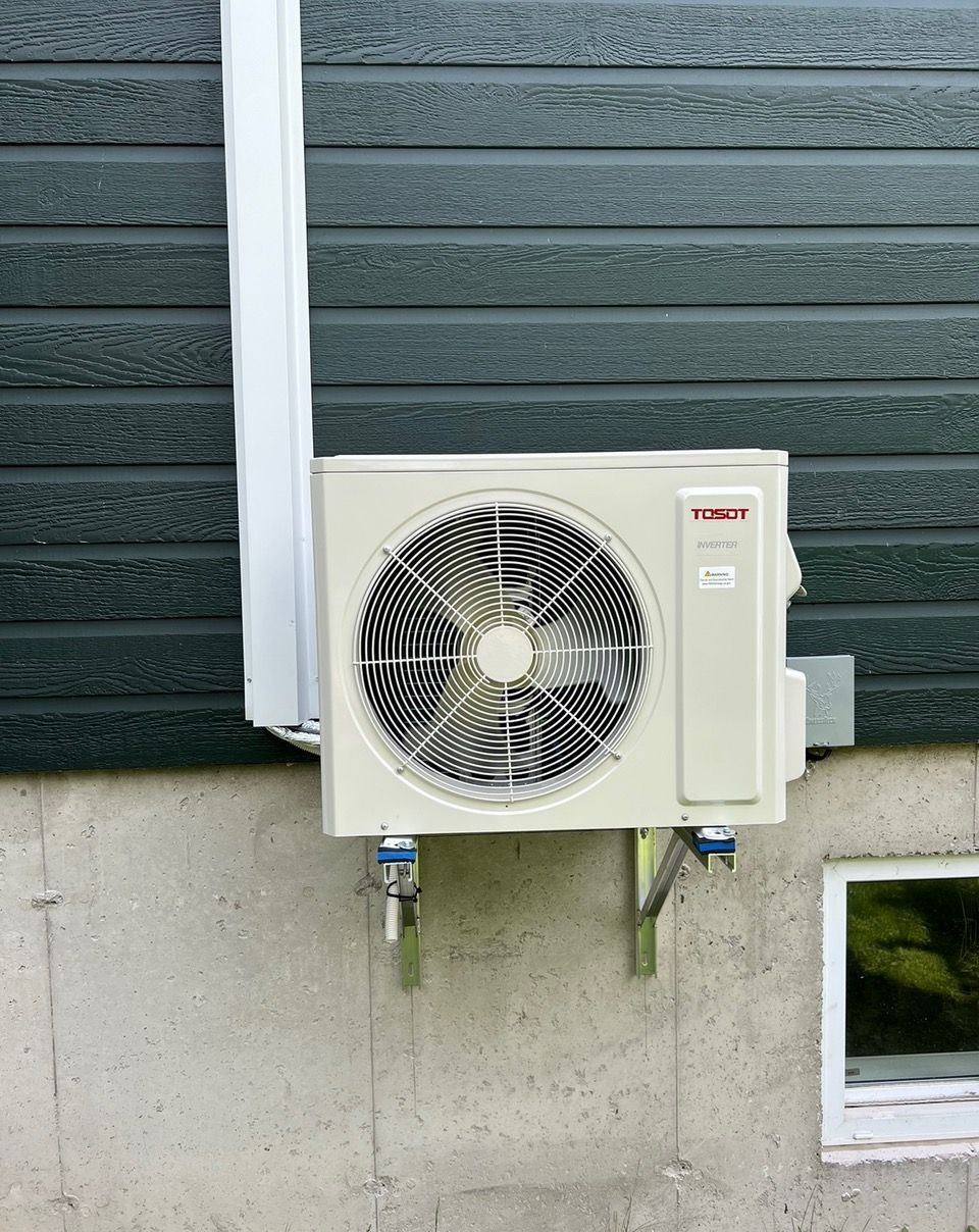 Un climatiseur blanc est monté sur le côté d'un bâtiment à côté d'une fenêtre.