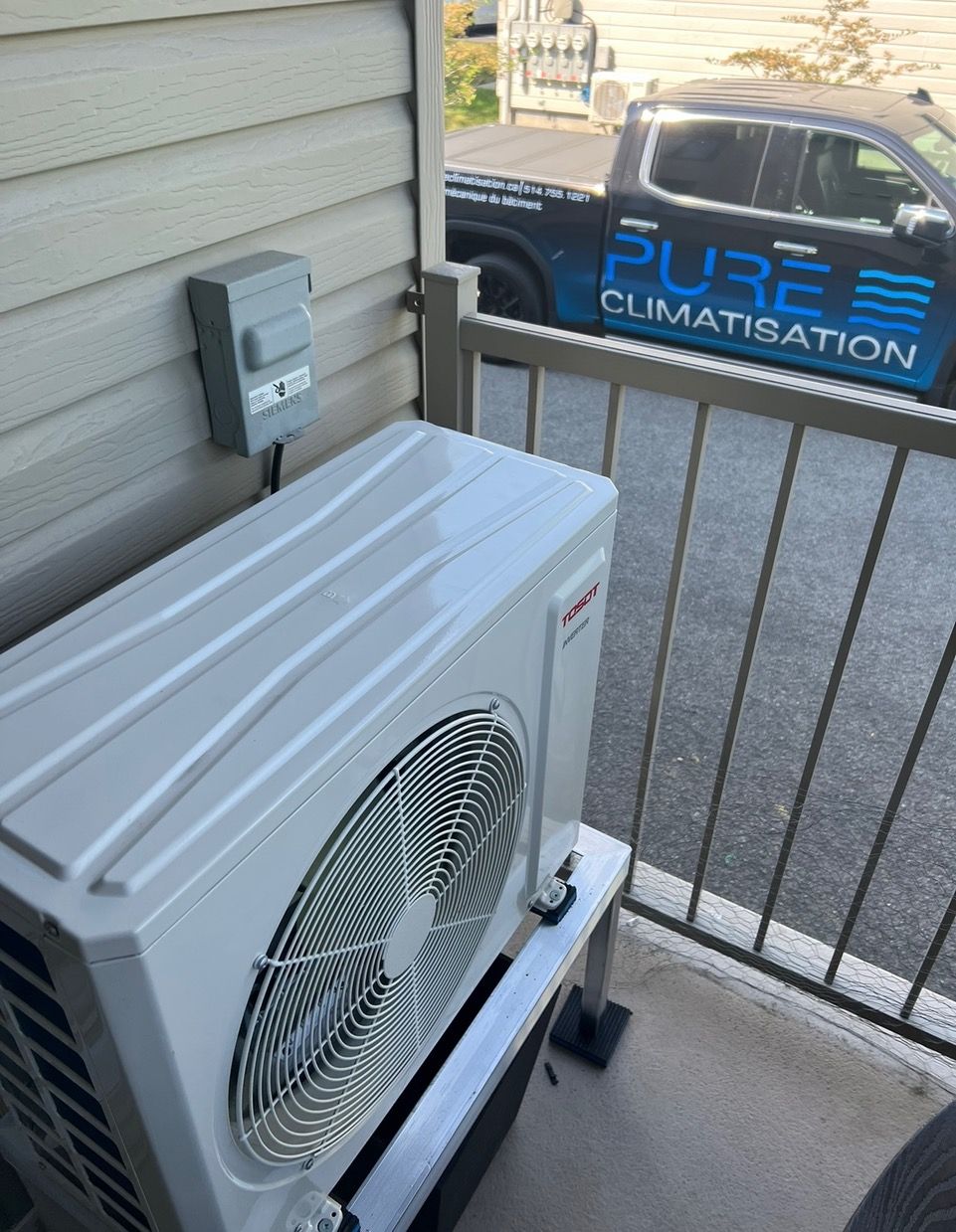 Un climatiseur blanc est posé sur un balcon à côté d'un camion sur lequel est écrit Pure Climatisation.
