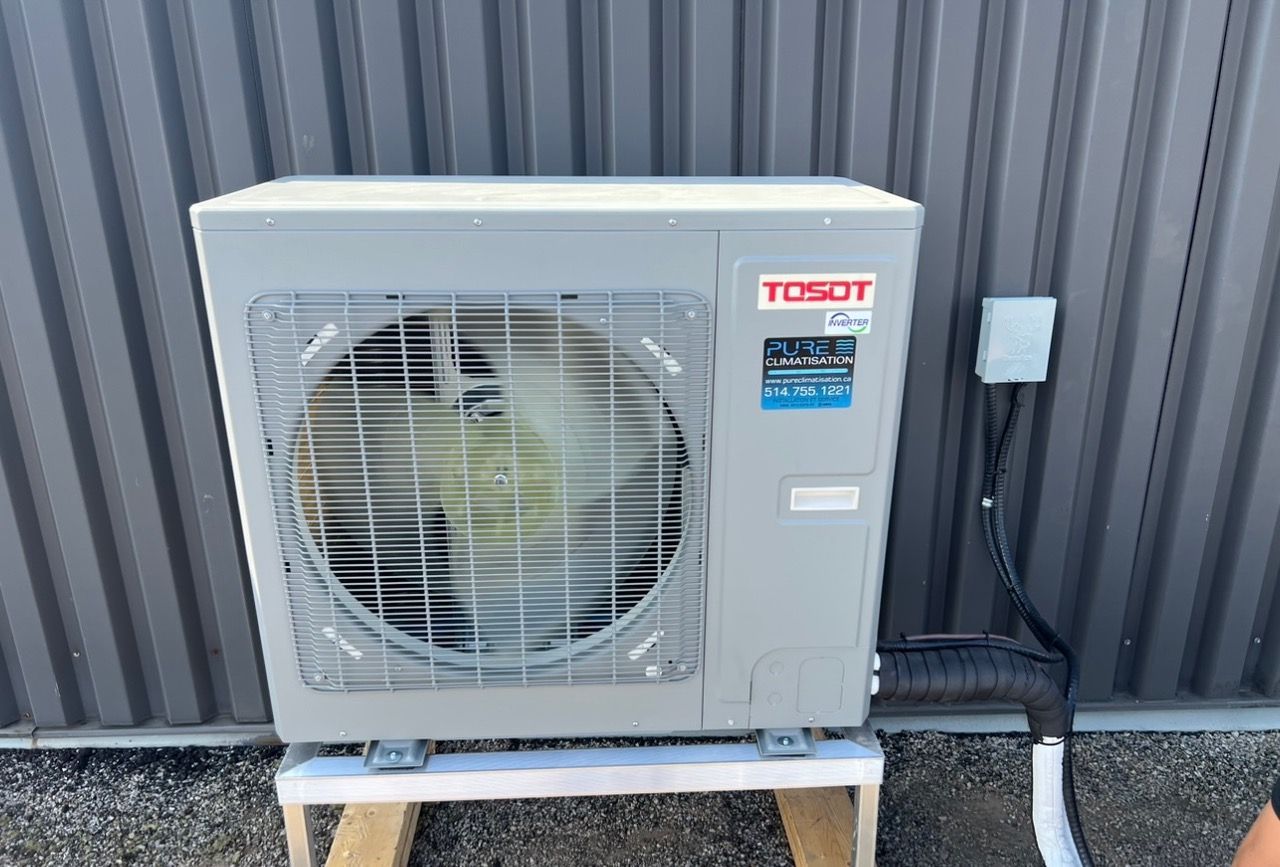 Un grand climatiseur est posé sur un support en bois à l'extérieur d'un bâtiment.