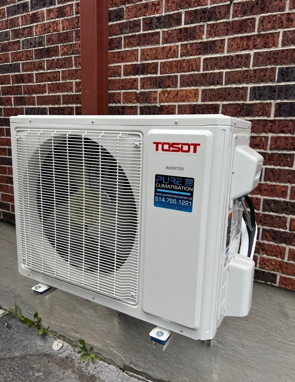 Un climatiseur Tosot est installé à l'extérieur d'un bâtiment en briques.
