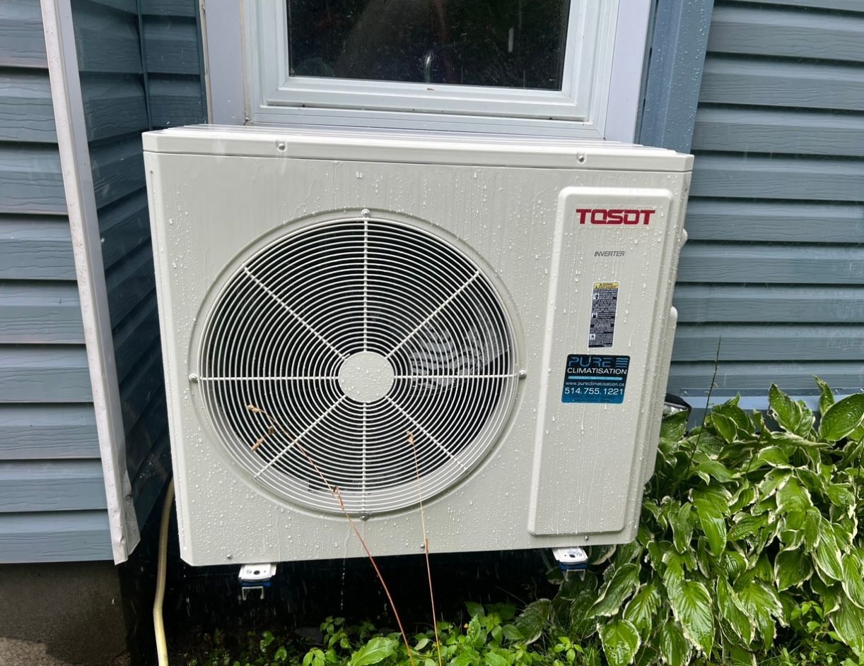 Un climatiseur tosot est placé à l'extérieur d'une maison à côté d'une fenêtre.