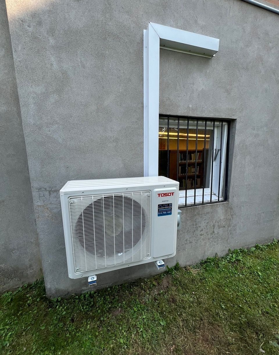 Un climatiseur blanc est monté sur le côté d'un bâtiment à côté d'une fenêtre.
