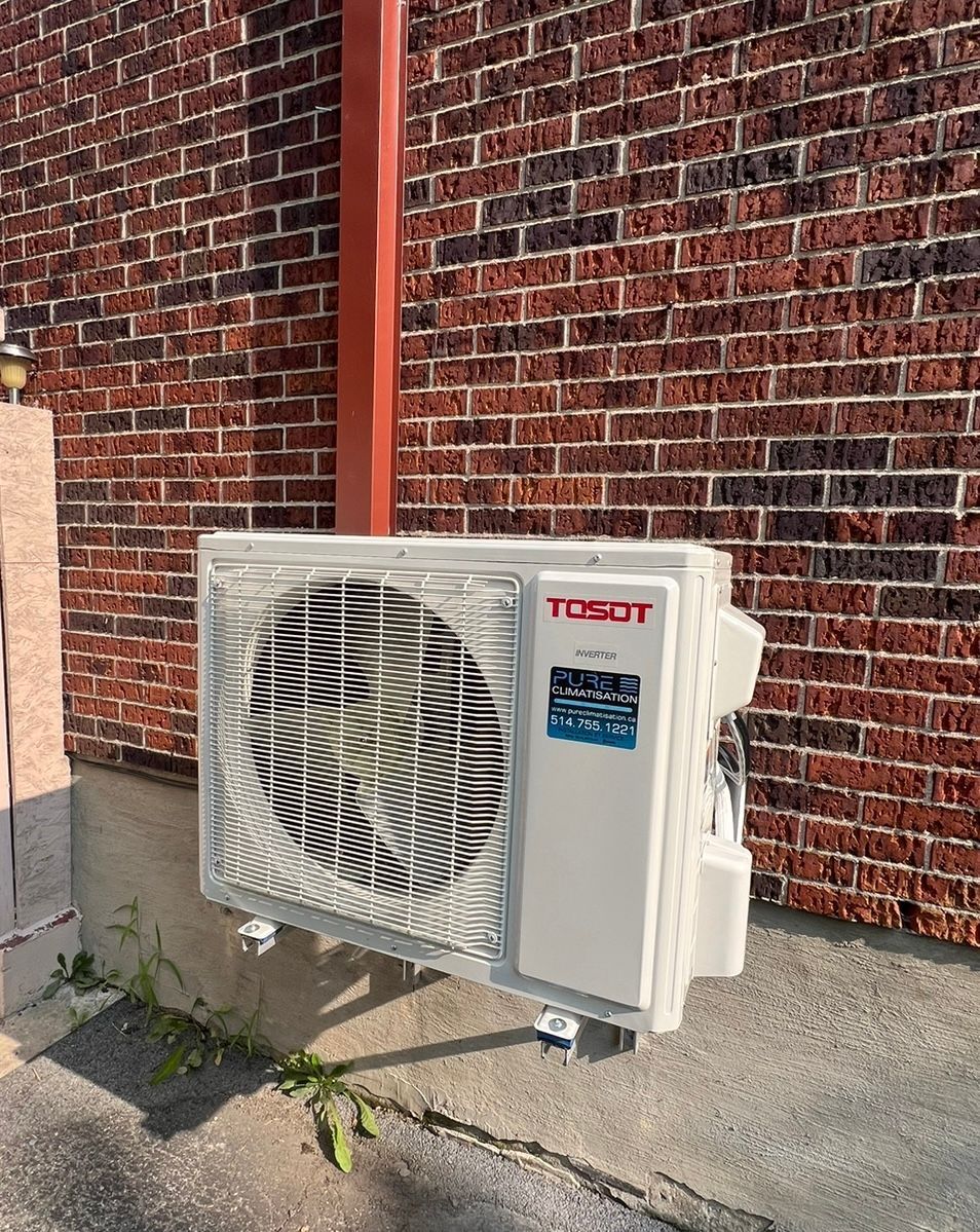 Un climatiseur blanc est posé sur le côté d'un bâtiment en briques.