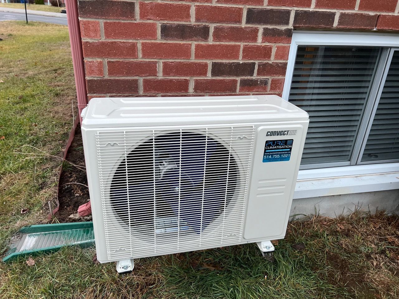 Un climatiseur blanc est posé sur le côté d'un bâtiment en briques.