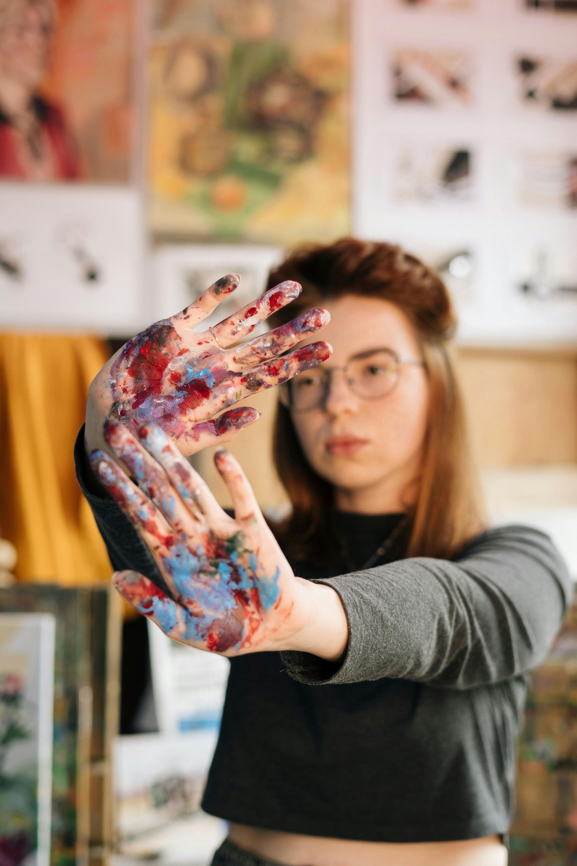 A painter in their studio with paint all over their hands and art on the walls