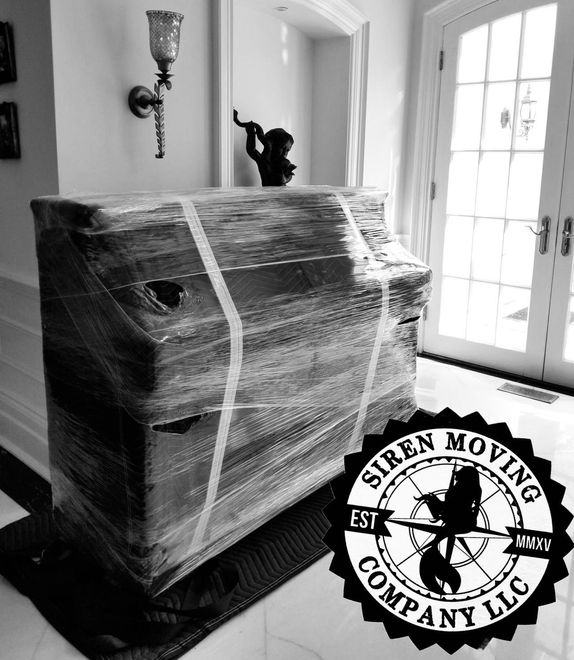 Piano wrapped in plastic, being moved. Siren Moving Company logo in the lower right corner.