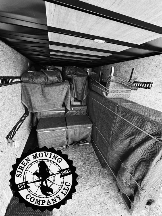 Inside of a moving truck, packed with wrapped furniture, boxes and goods. Siren Moving Company logo overlay.