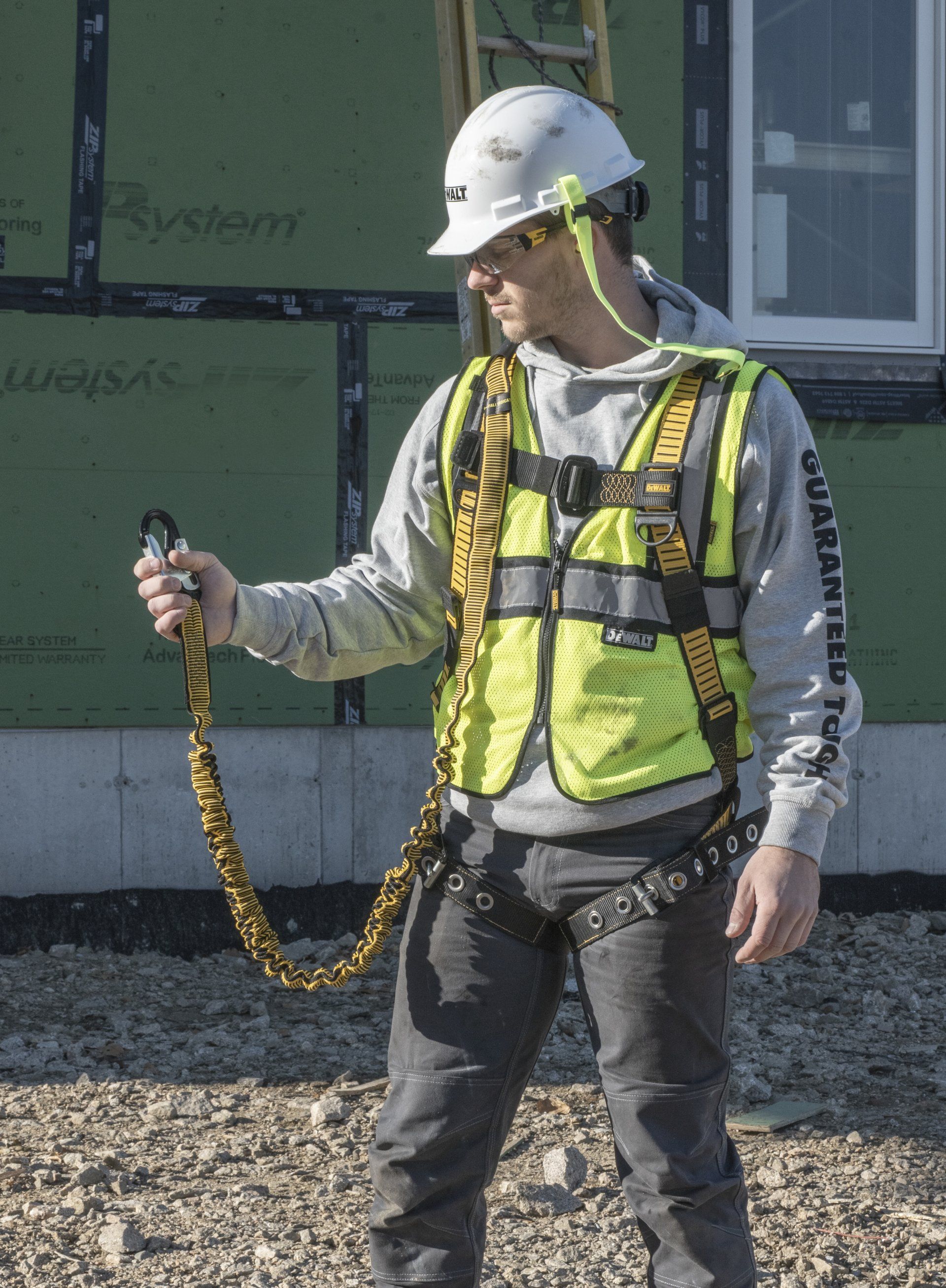 Construction worker in a safety harness holding a lanyard. He's wearing a helmet and a reflective vest.
