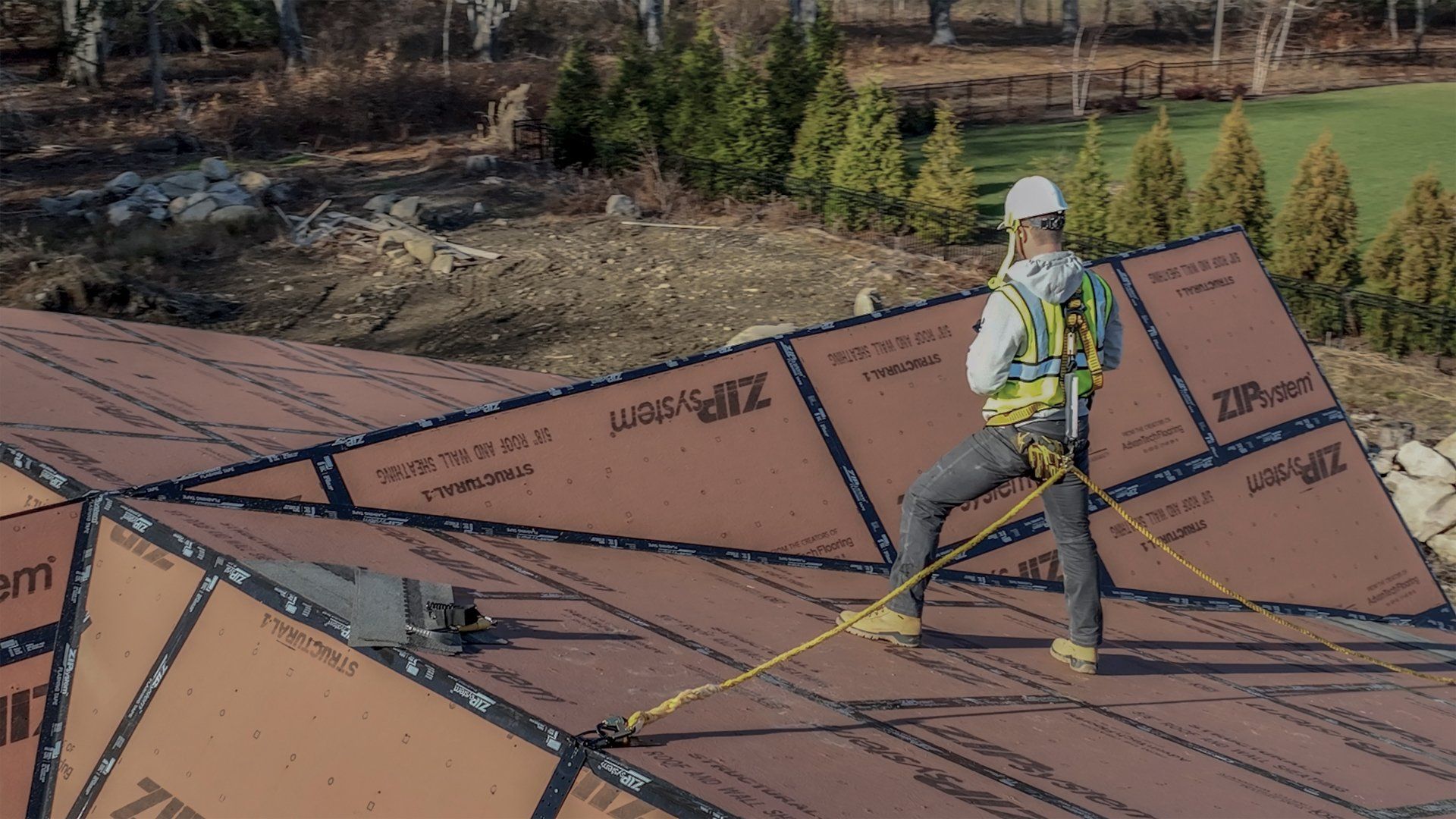 Construction worker on a roof wearing a harness and safety gear.
