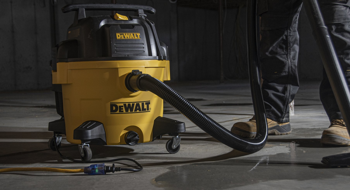 Yellow DeWalt wet/dry vacuum on wheels with hose being used on a concrete floor.