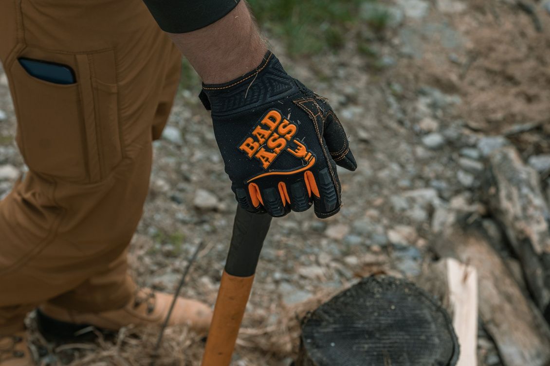 Man in brown pants and work glove holding an axe; glove has “BAD ASS” text.