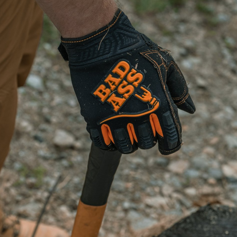 Man in brown pants and work glove holding an axe; glove has “BAD ASS” text.