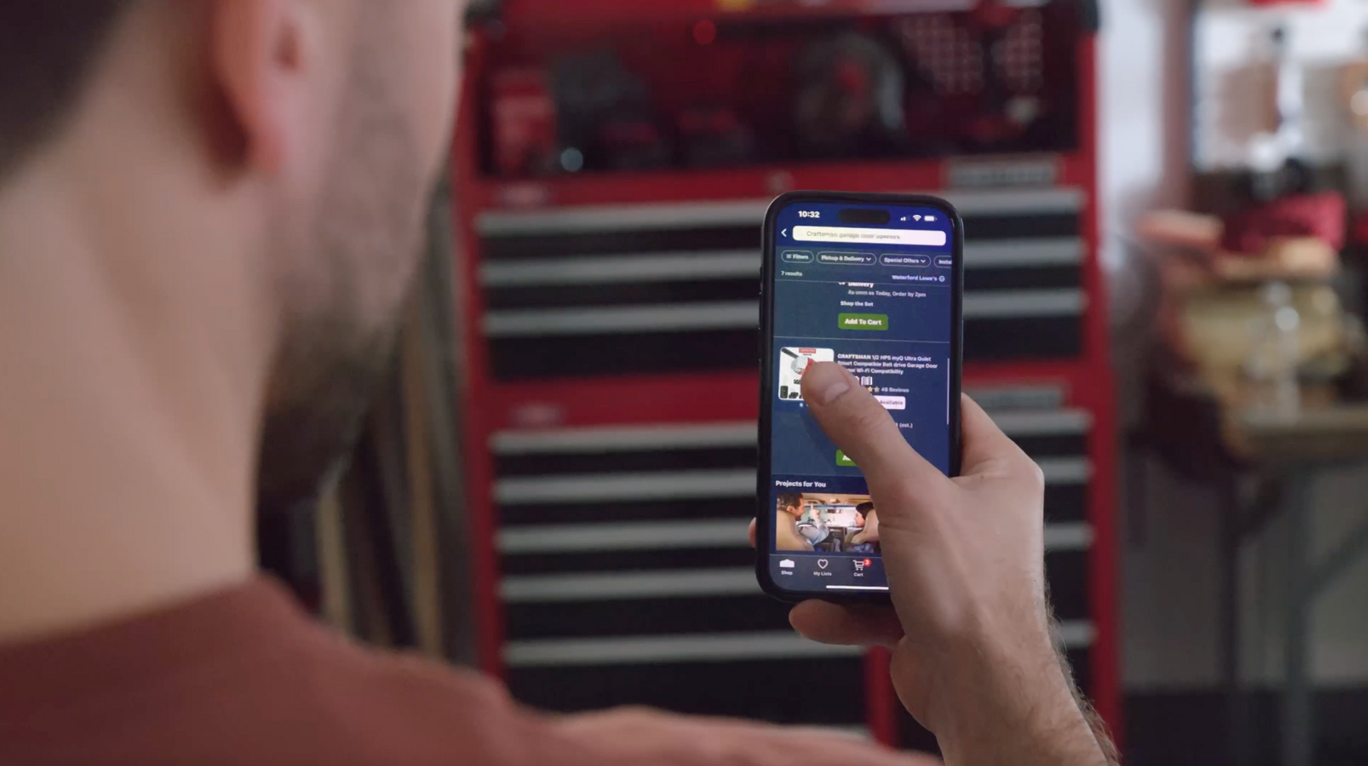 Man using a smartphone in front of a red toolbox in a garage, scrolling on a screen.