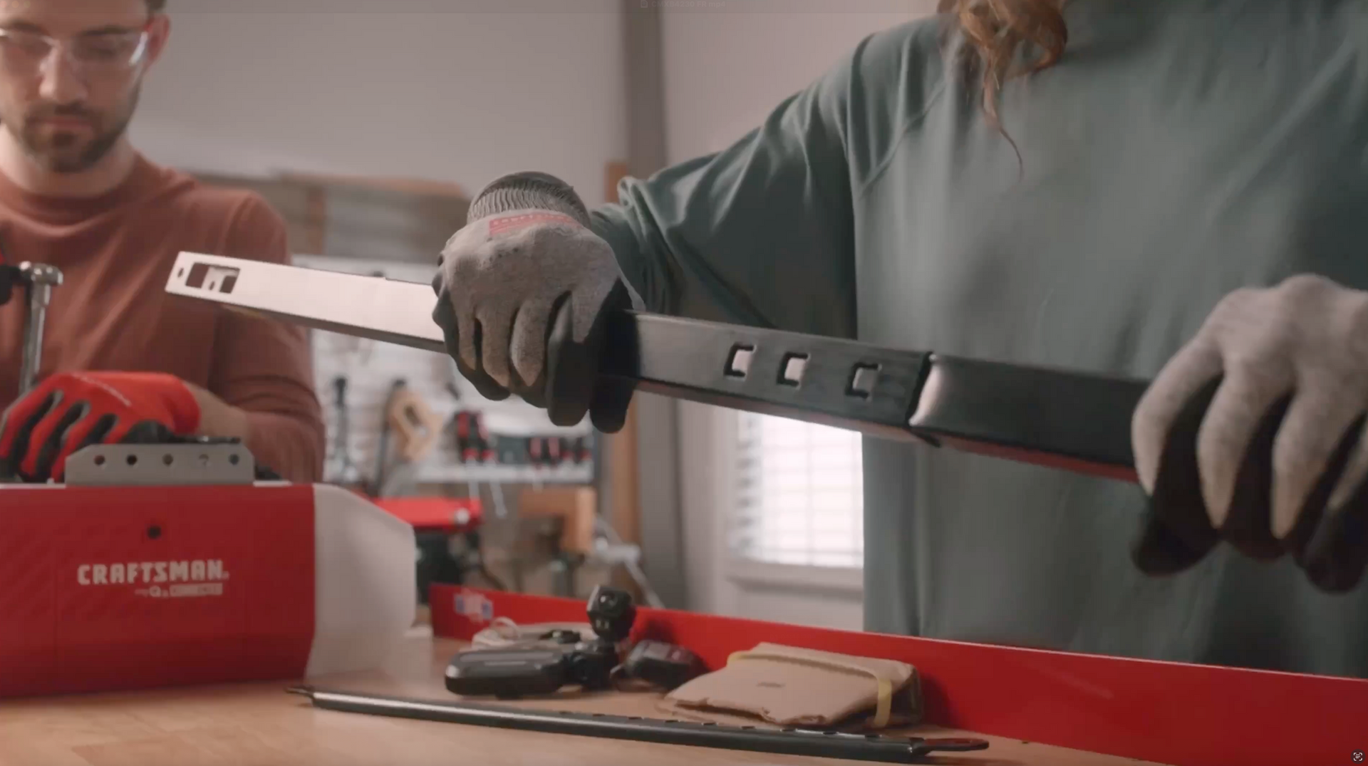 Two people assembling a black garage door opener rail in a workshop; one holds the rail.