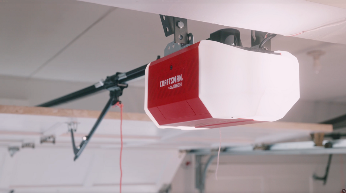 Garage door opener, red and white motor unit attached to ceiling, in a garage.
