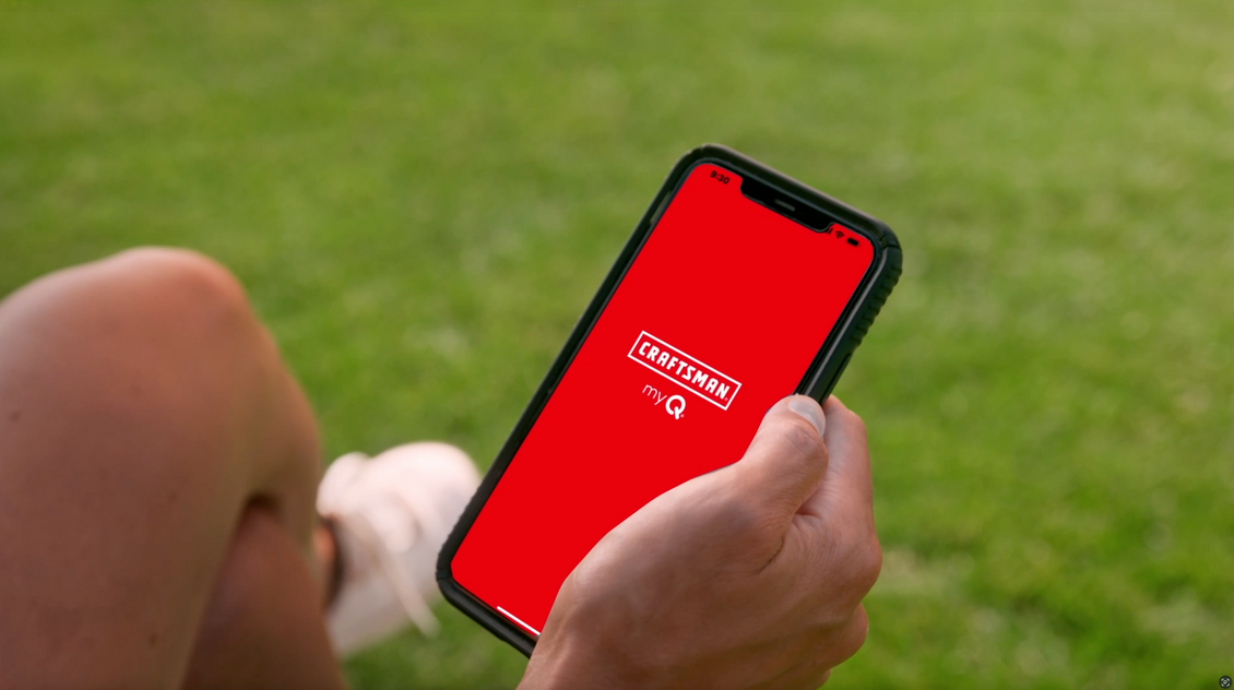 Person holding phone with red screen and white logo outdoors on grass.