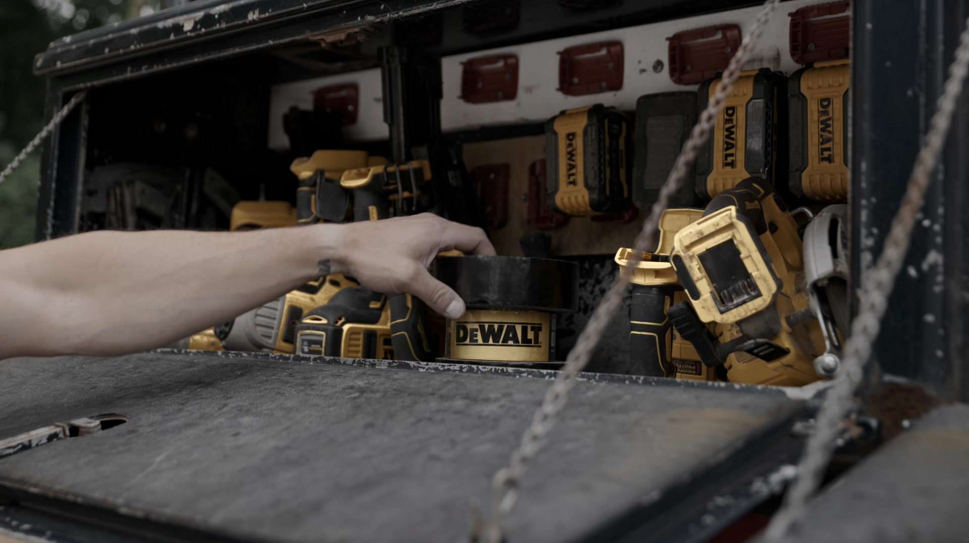A hand reaching into a black truck bed full of DeWalt power tools, batteries, and accessories.