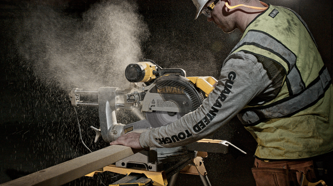 Construction worker cutting wood with a saw; dust flying. Wearing safety gear, indoors.