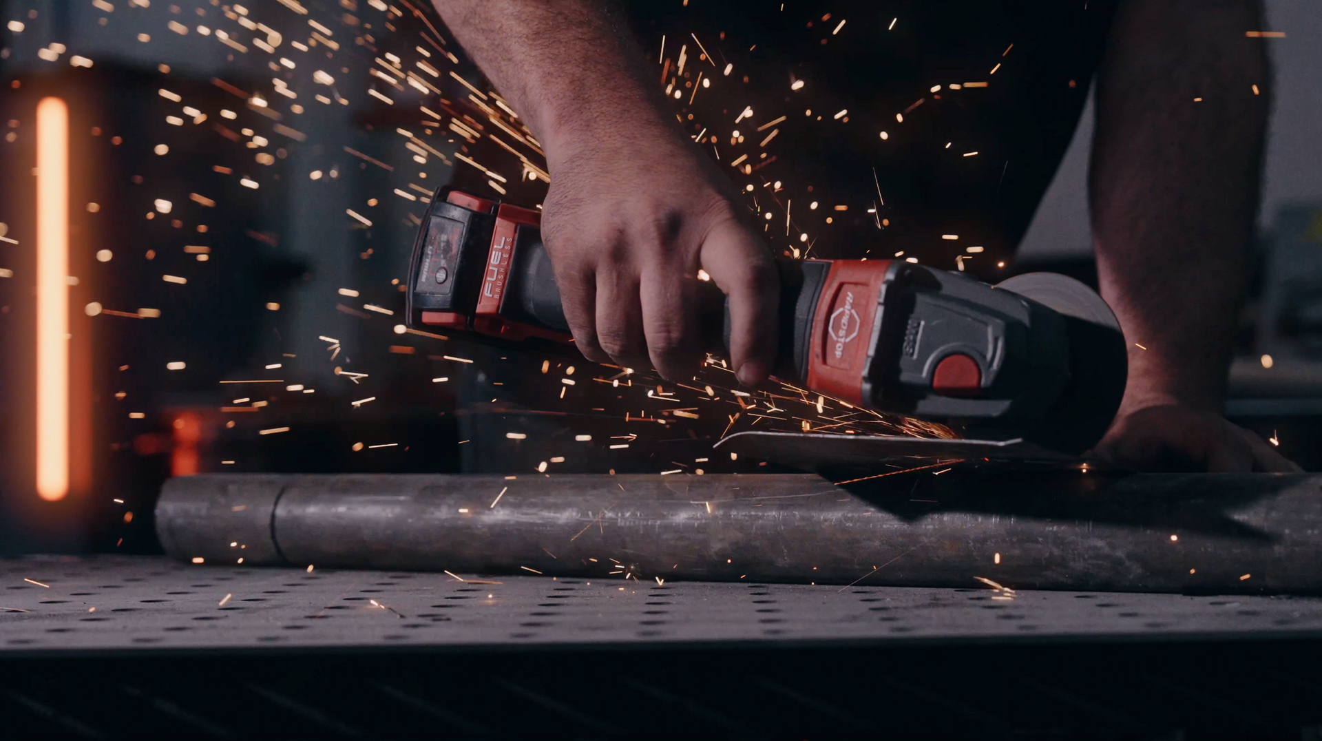 Person using an angle grinder, sparks flying, cutting metal pipe.