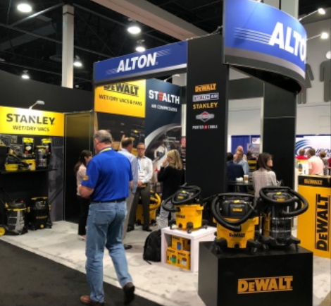People at the DeWalt booth in a trade show, with yellow and black vacuum cleaners on display.