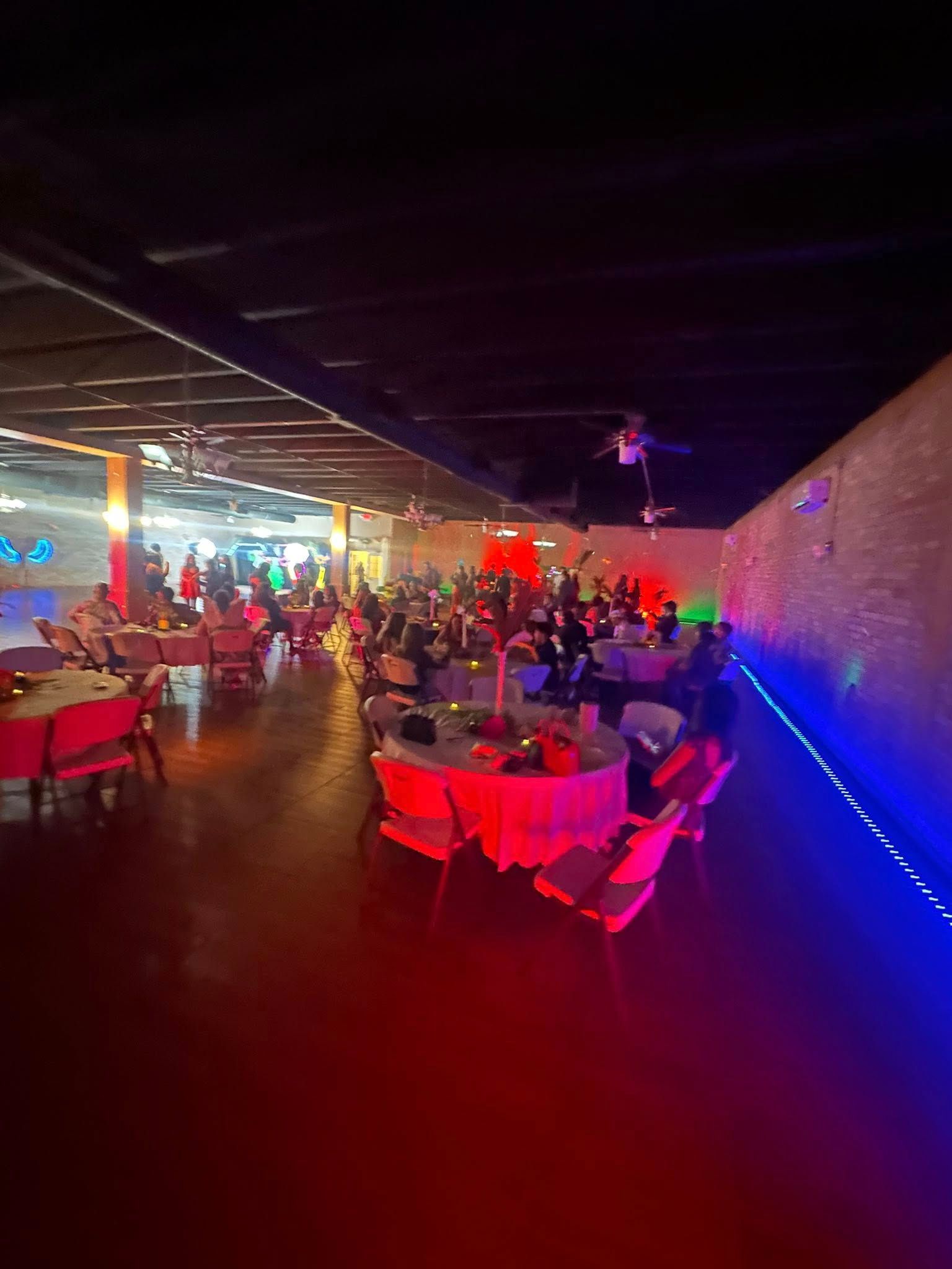 Party with people gathered at tables in a large, dimly lit room with red and blue lighting.