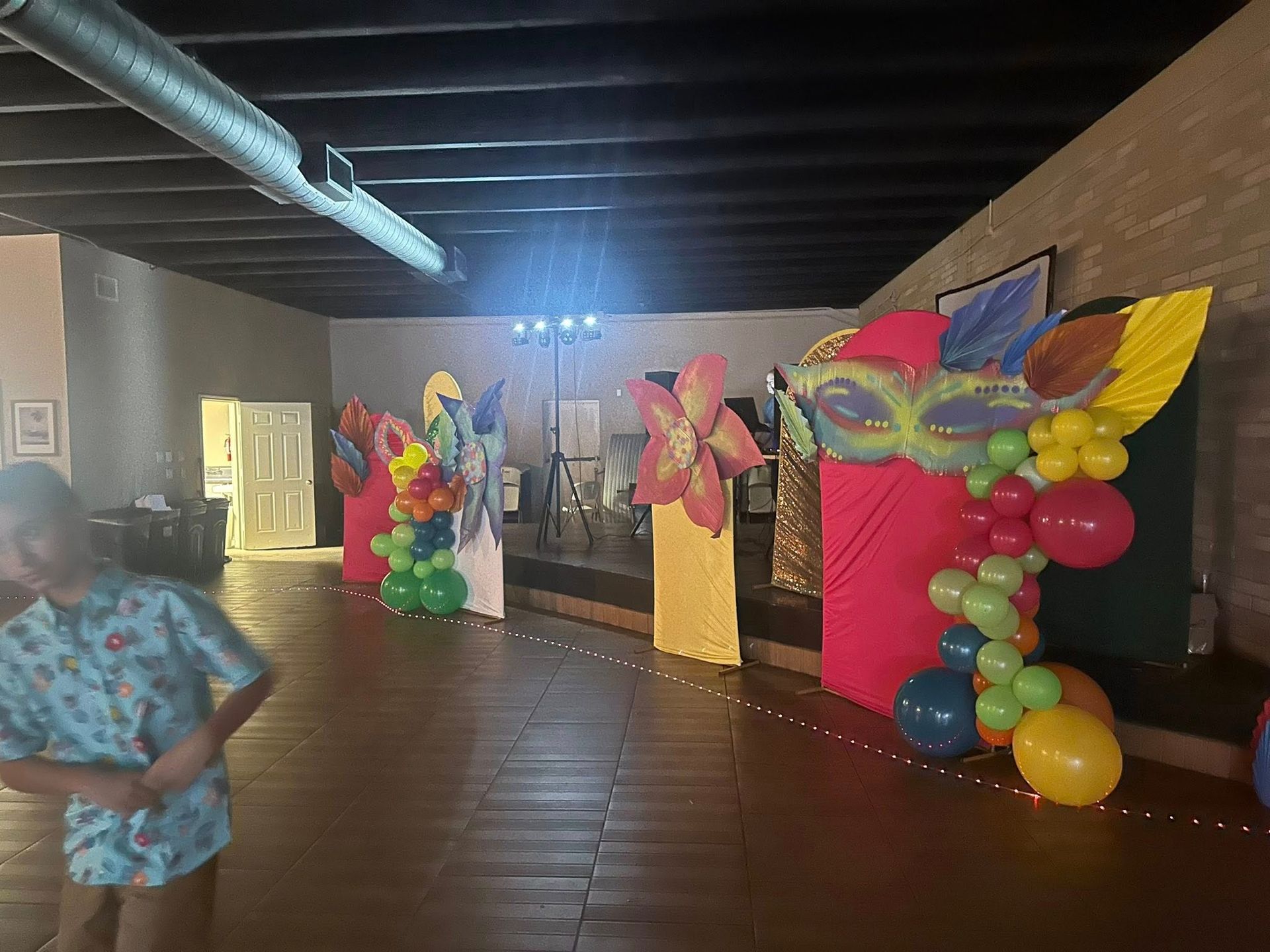 Decorated indoor space with colorful party decorations, balloons, and a person in the foreground.