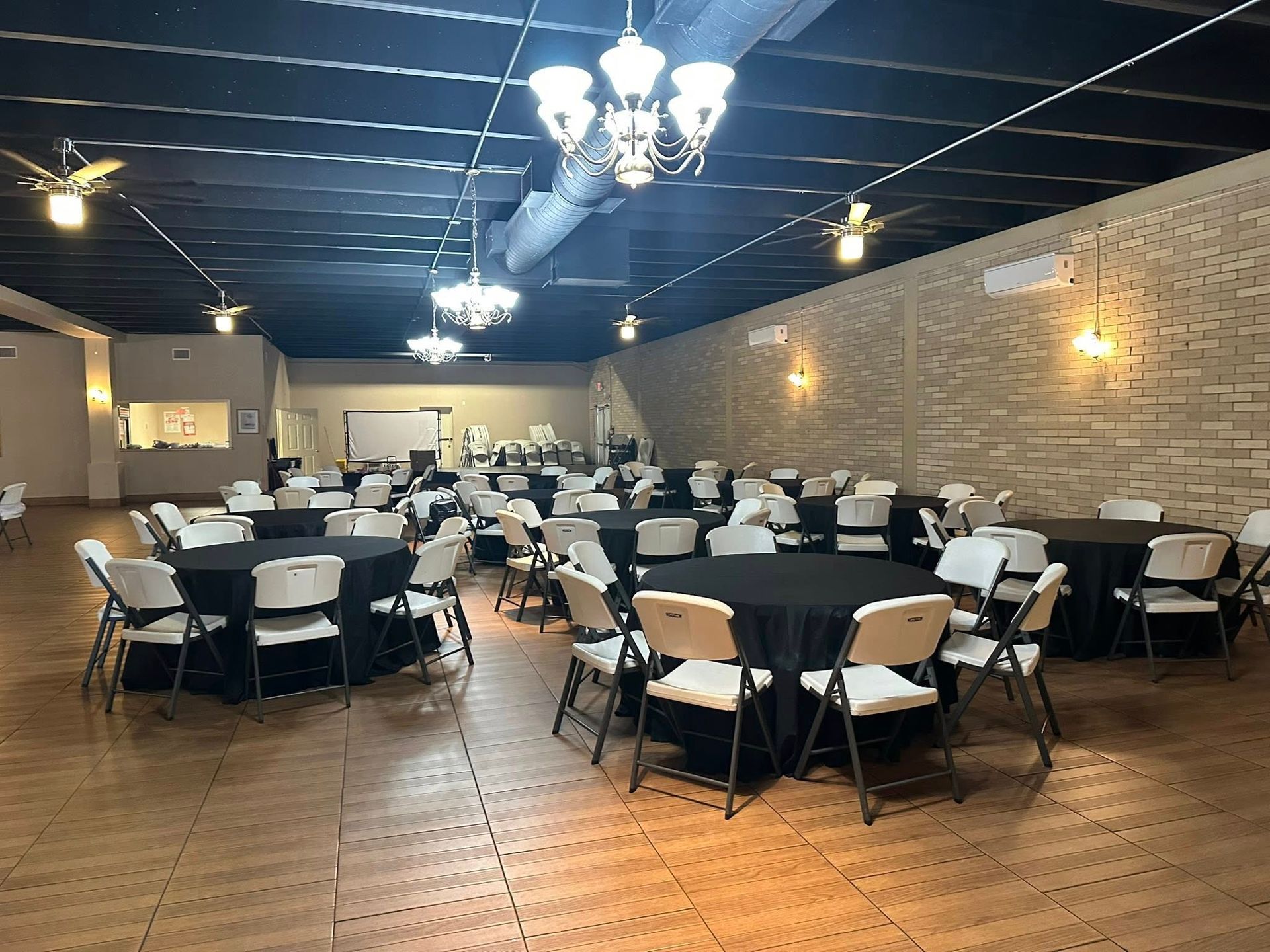 Event space with round tables covered in black linens, surrounded by white chairs; neutral color palette.