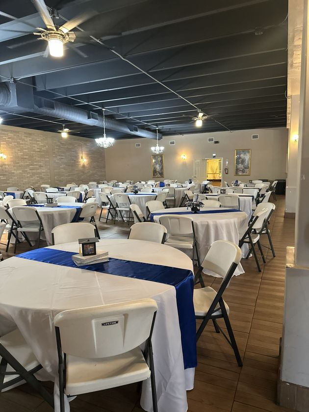 Reception hall with white tables, blue runners, and white folding chairs.