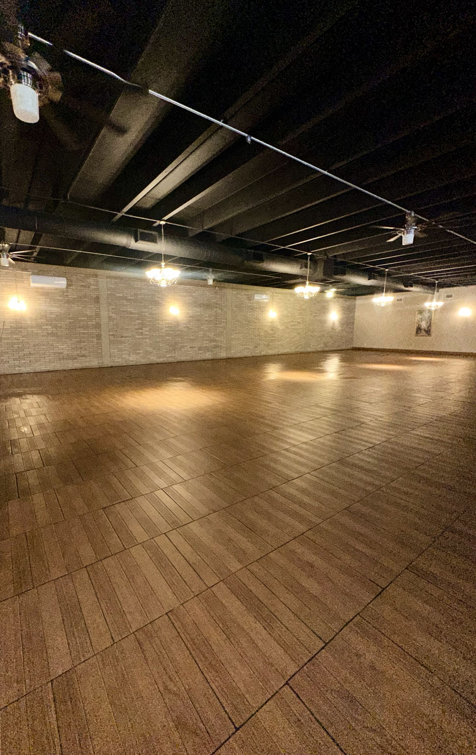 Empty dance studio with brown flooring, brick walls, and dim lighting.