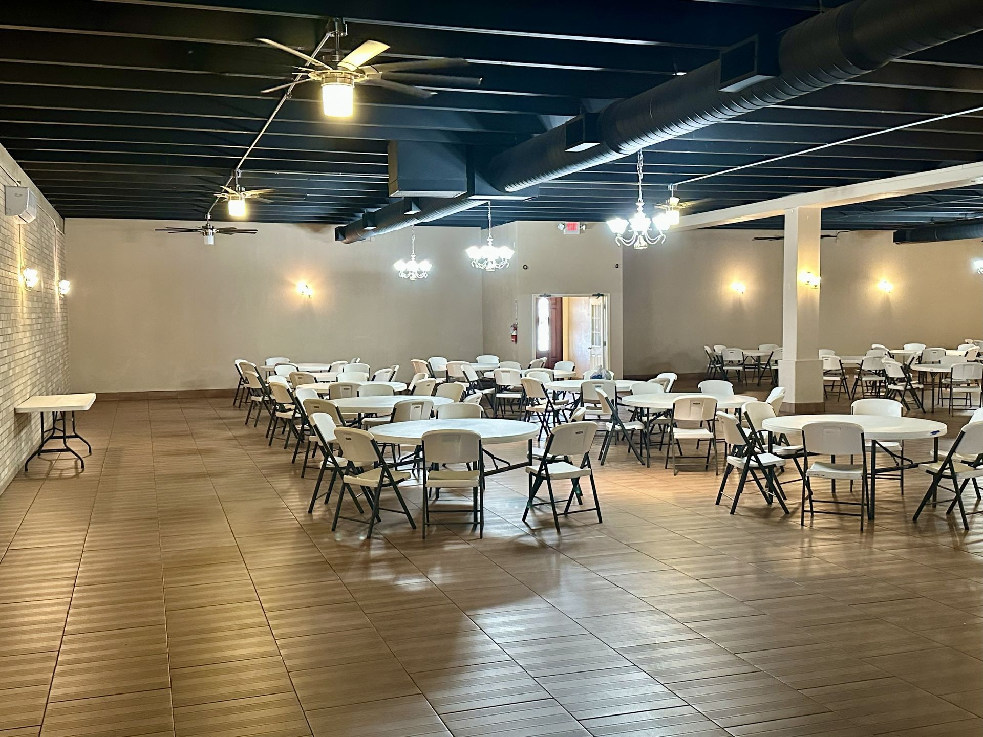 Large event hall with white tables and chairs; black ceiling with hanging lights, off-white walls.
