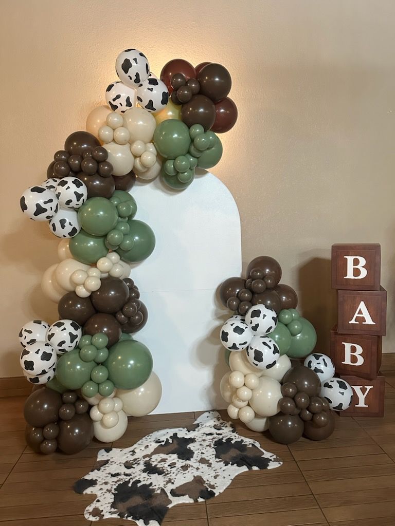 Balloon arch with a cowhide rug and block letters spelling BABY.
