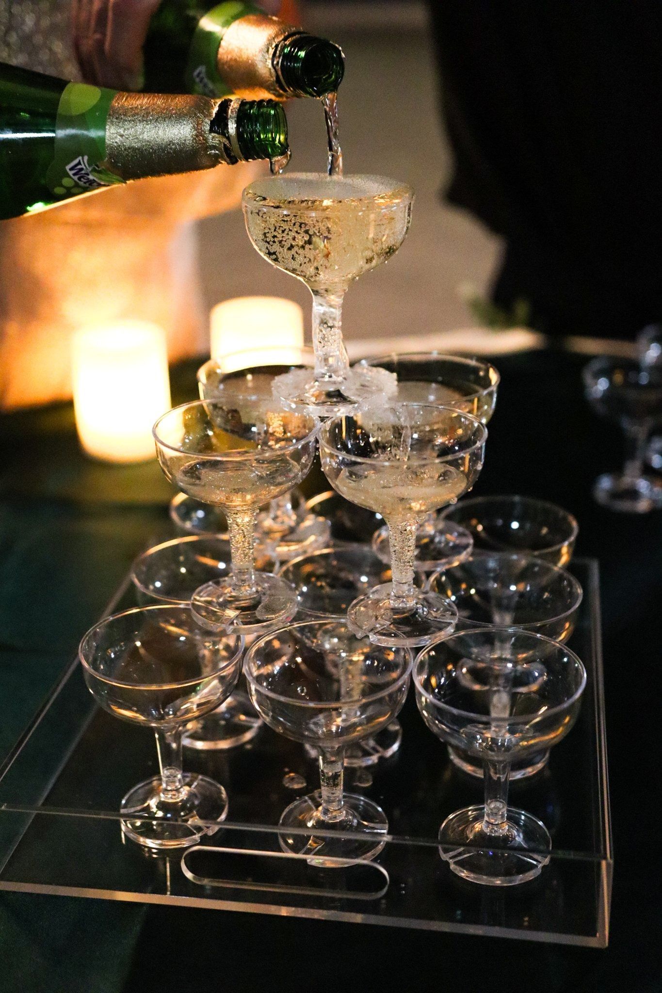 Champagne glasses stacked in a pyramid, being poured from a bottle, on a mirrored tray.