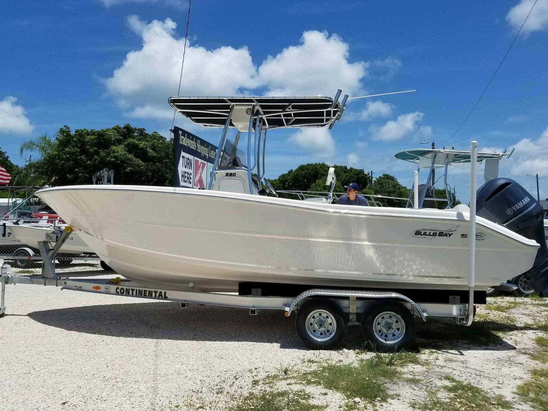 A white boat is parked on a trailer in a gravel lot.