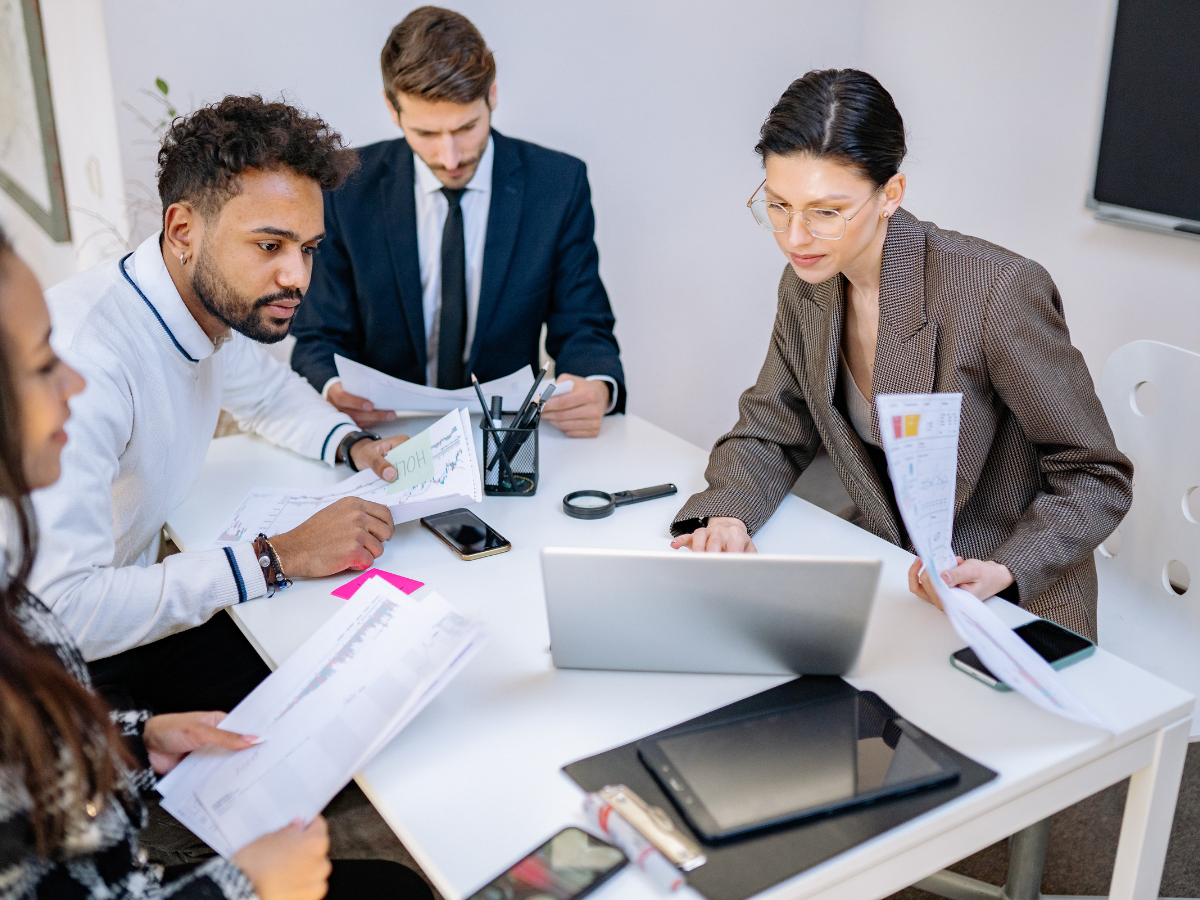 Four people at a table reviewing documents and a laptop in an office setting.