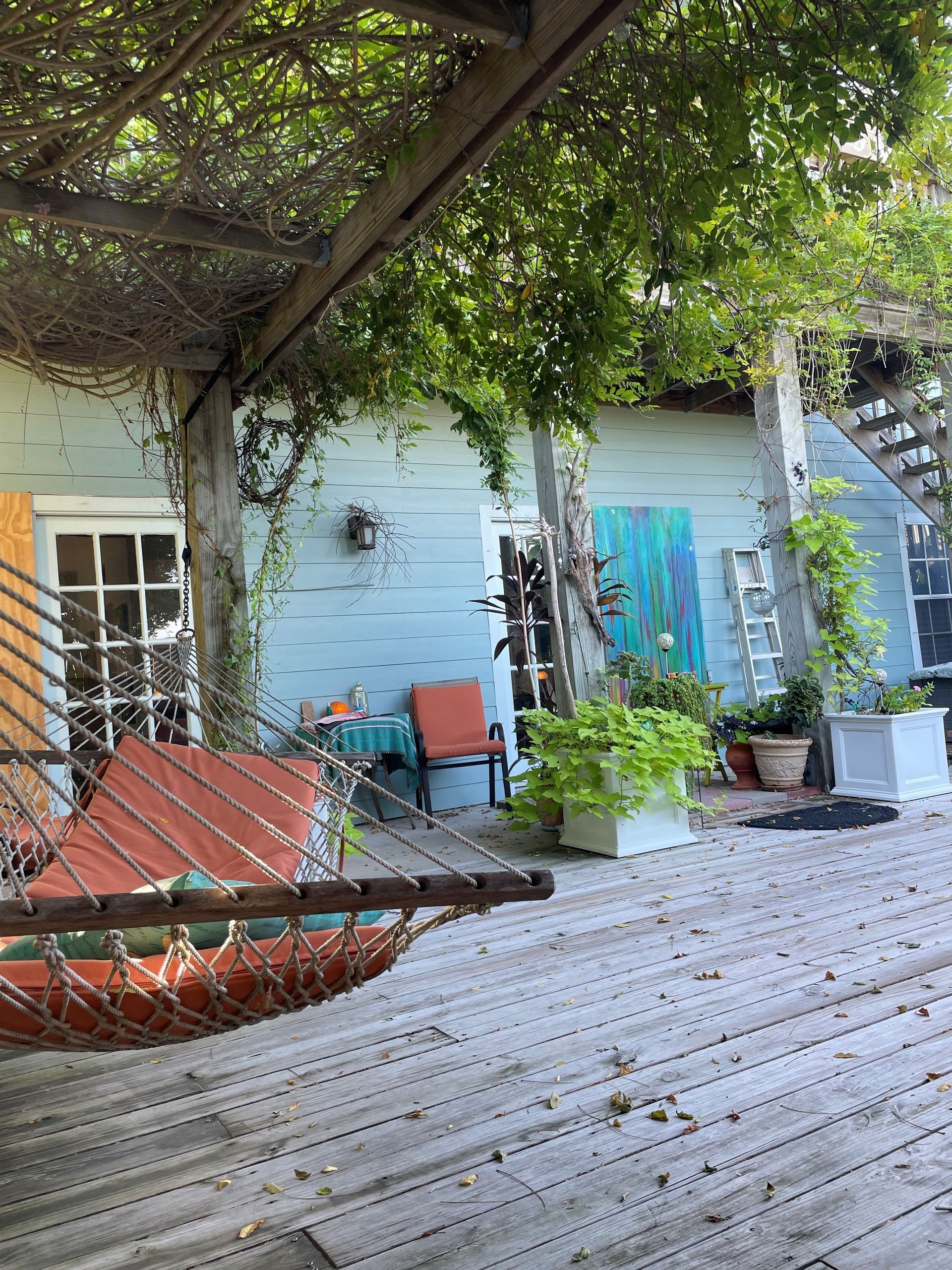 A hammock is hanging on a wooden deck in front of a house.