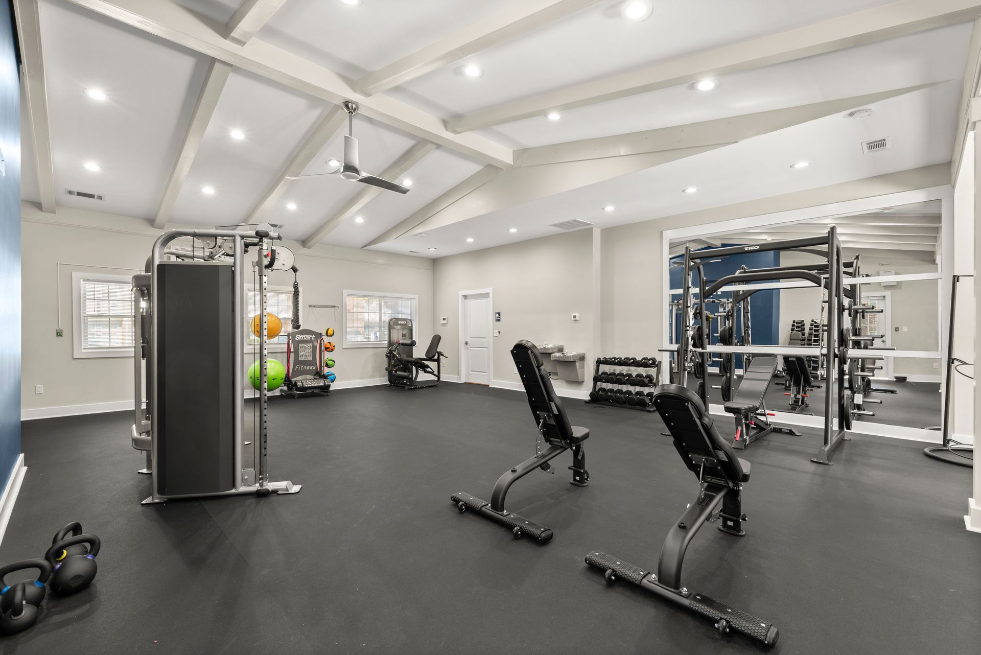 Gym interior with weight machines, free weights, and benches on black rubber flooring, under a white vaulted ceiling at The Arbors at Smyrna, offers apartments in Cobb County.