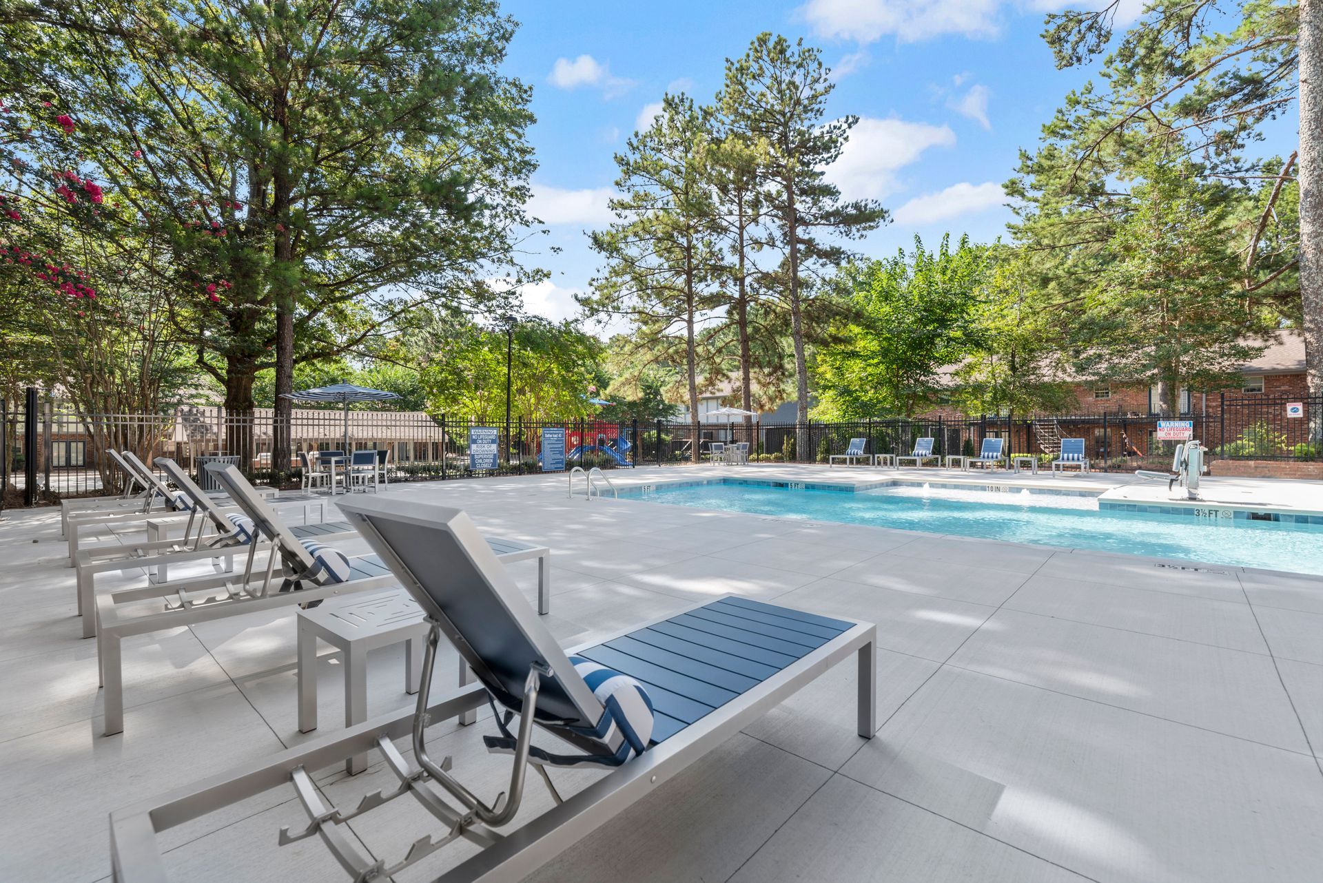 Poolside scene with lounge chairs, a pool, and trees under a blue sky at The Arbors at Smyrna, offers pet-friendly apartments in Smyrna, GA.