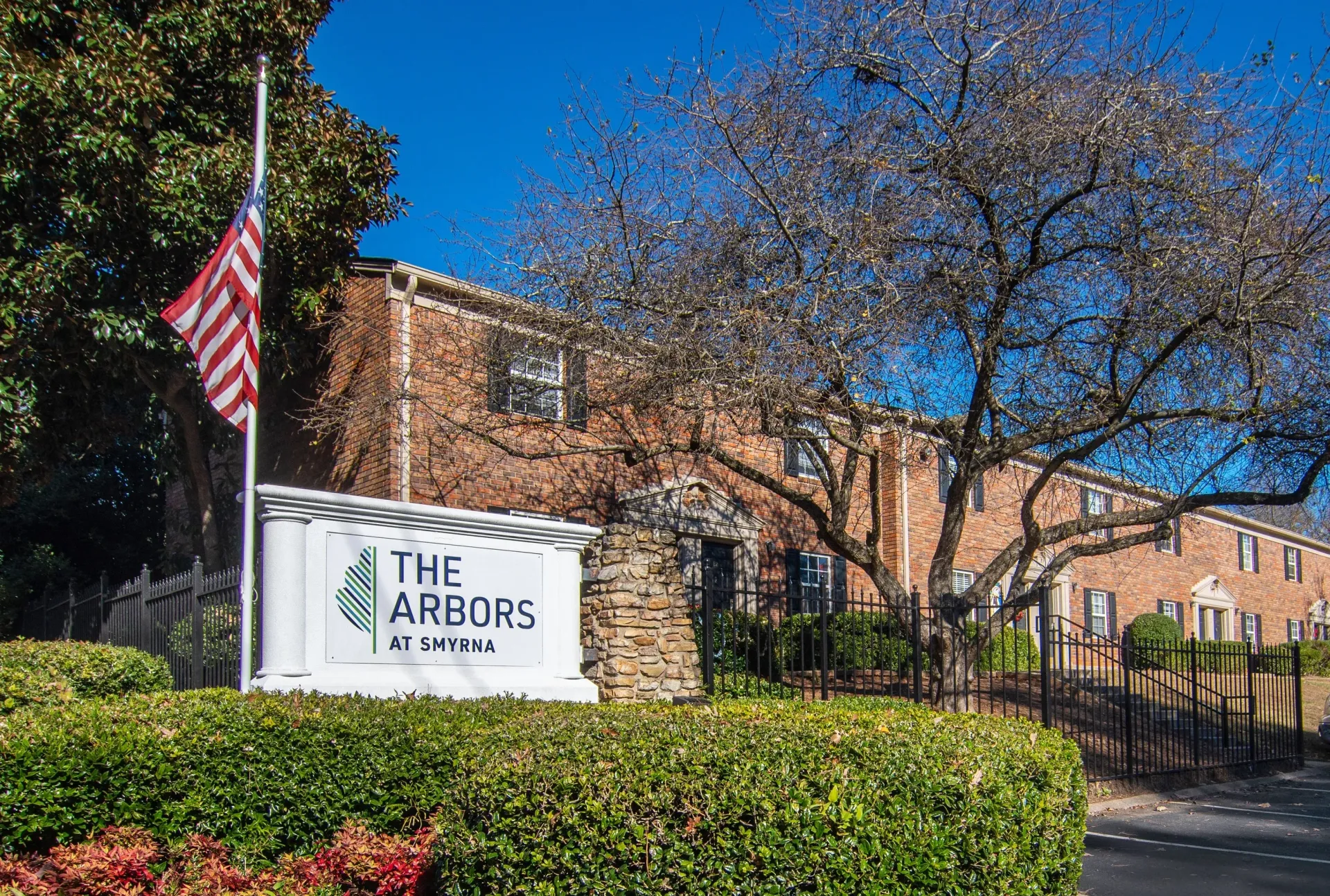 The Arbors apartment complex sign with a brick building and American flag against a blue sky.