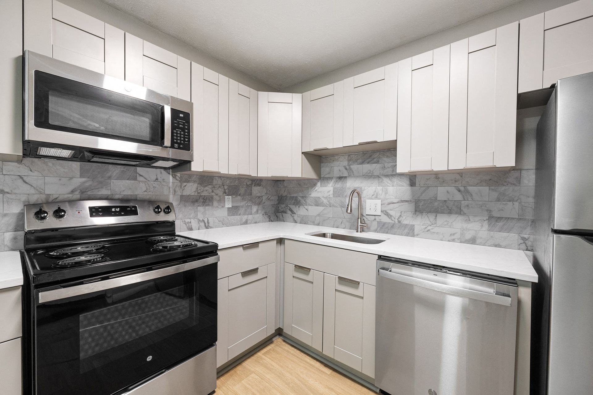 Kitchen with light gray cabinets, stainless steel appliances, and gray tiled backsplash at The Arbors at Smyrna, offers townhomes for rent in Smyrna, GA.