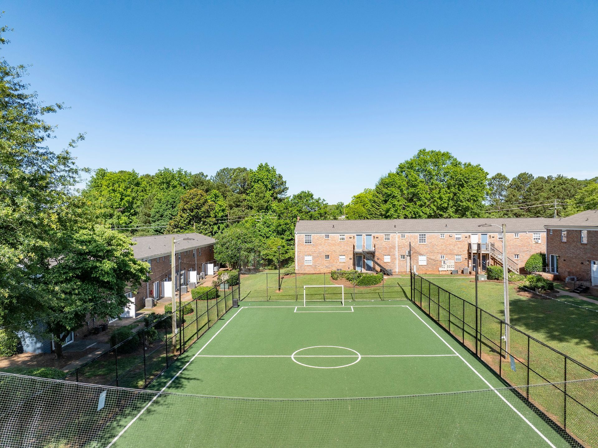 Soccer field between two-story brick apartment buildings, sunny day, green field, black fence.