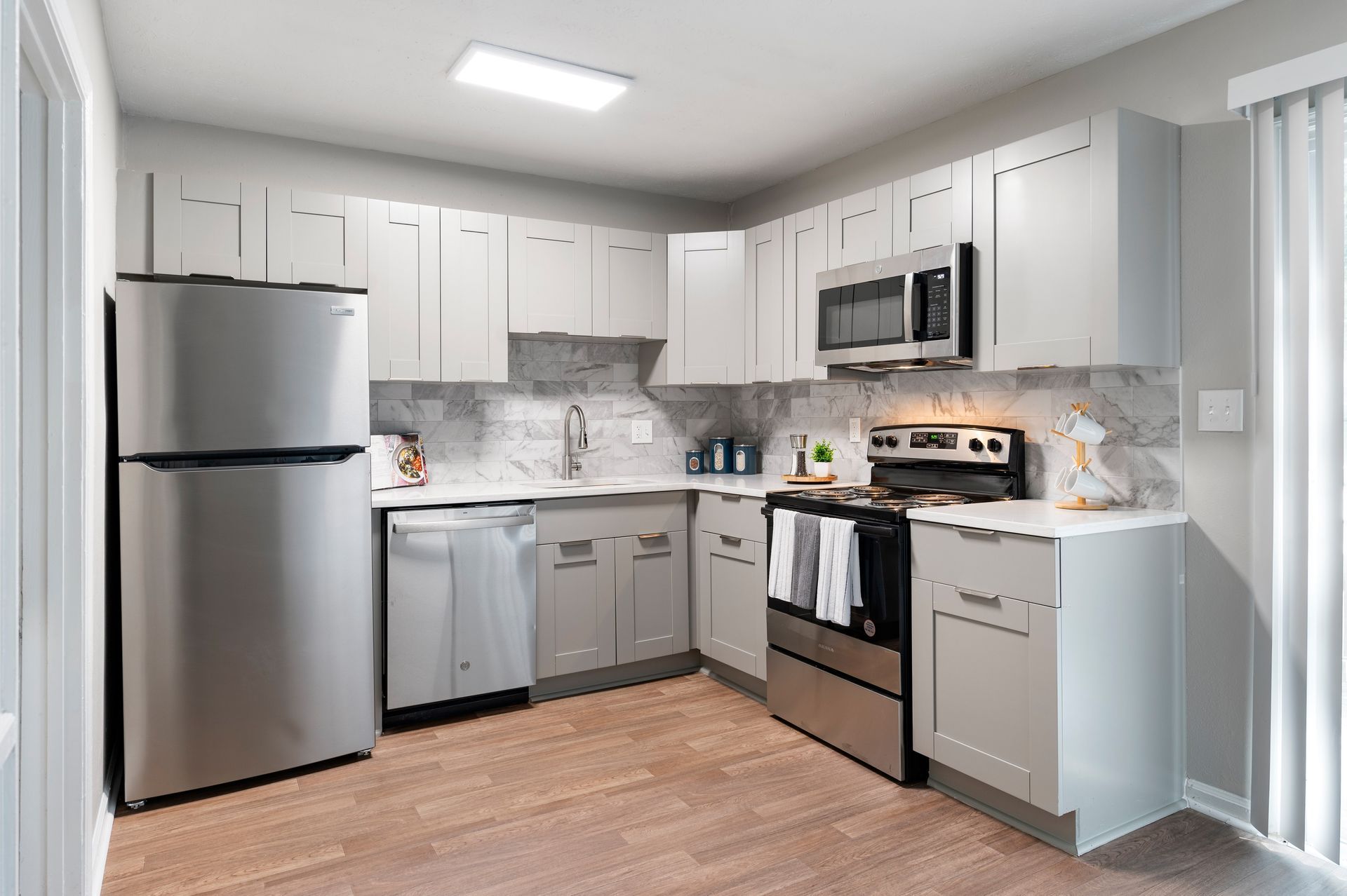 Modern kitchen with stainless steel appliances, grey cabinets, and wood-look flooring.