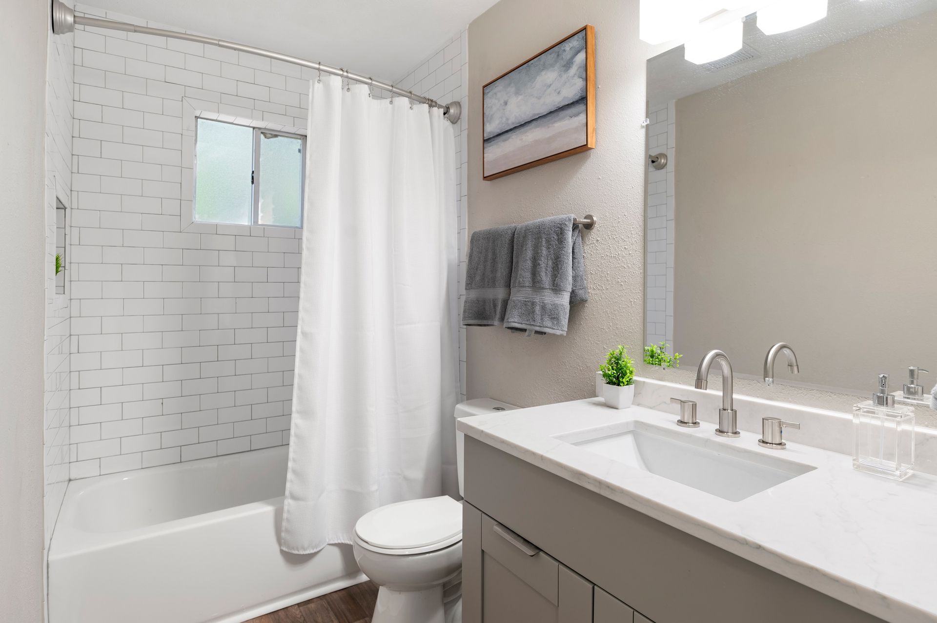 Bathroom with white subway tile, white shower curtain, grey vanity, and artwork at The Arbors at Smyrna, offers Smyrna townhomes for rent.