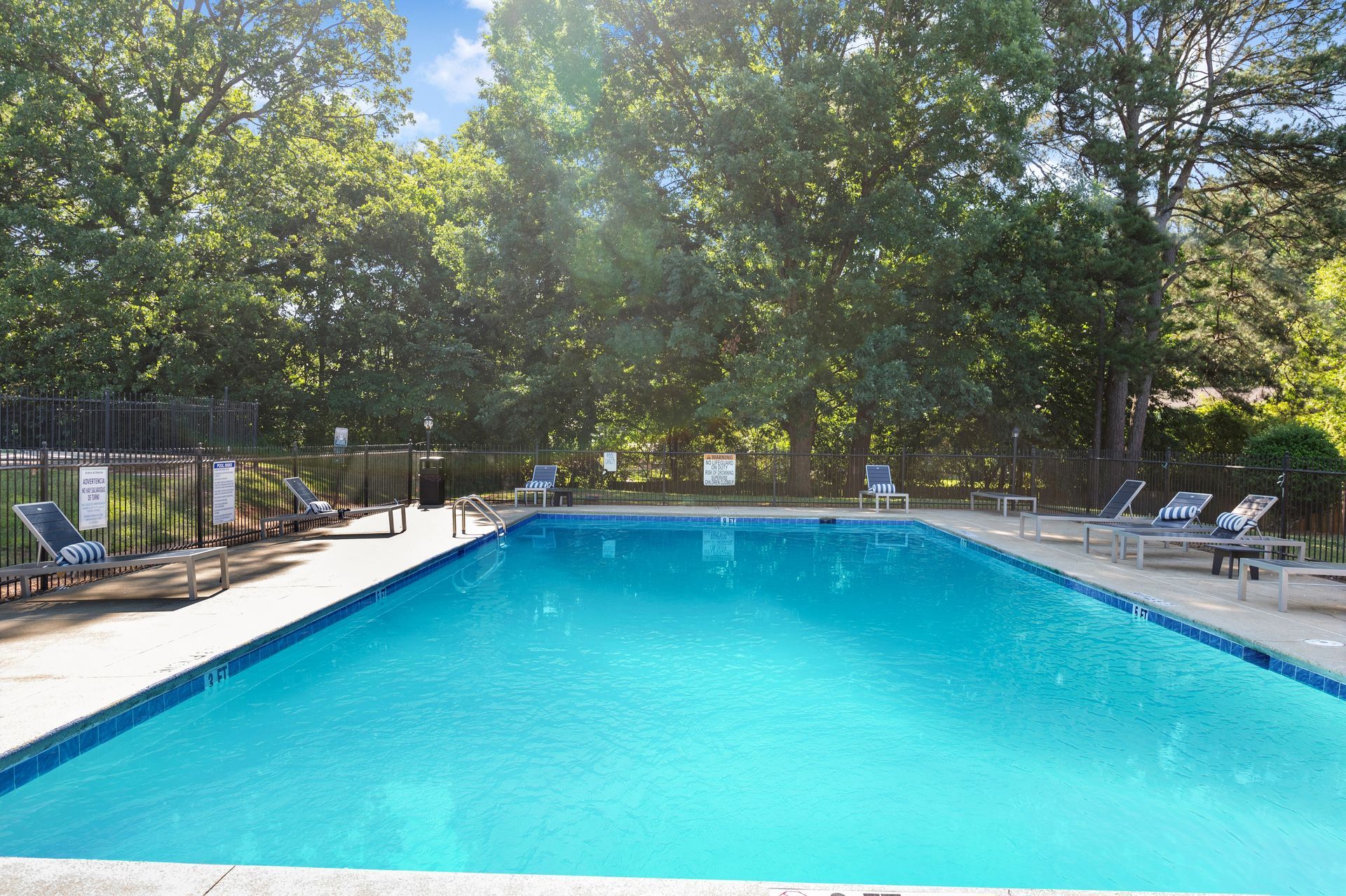 Swimming pool with lounge chairs, fenced with trees in the background. Blue water at The Arbors at Smyrna, offers apartments near Cumberland Mall in Smyrna, GA.