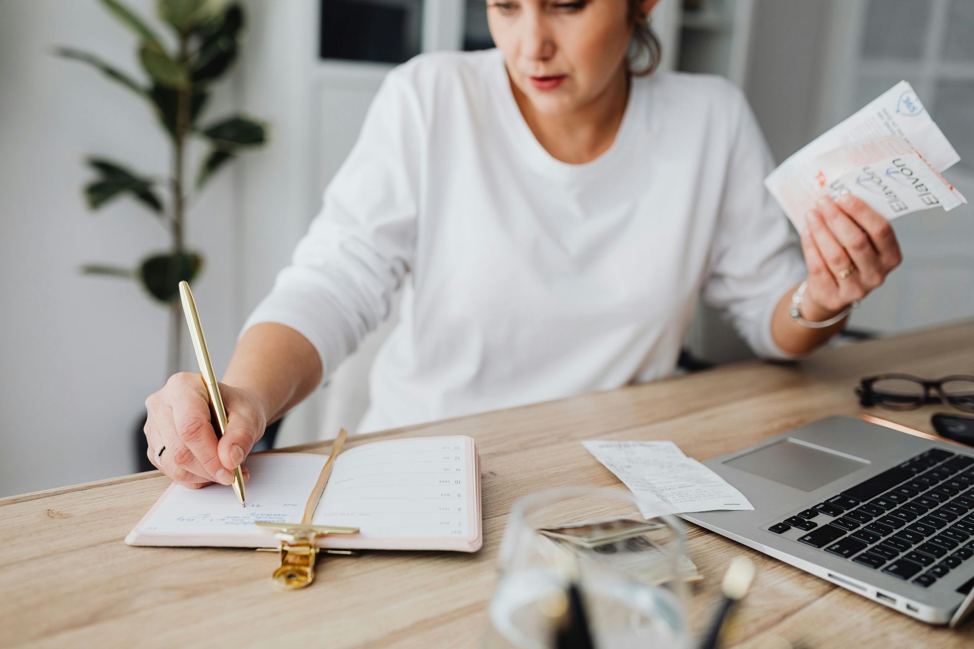 A woman is sitting at a desk writing in a notebook and holding a receipt.