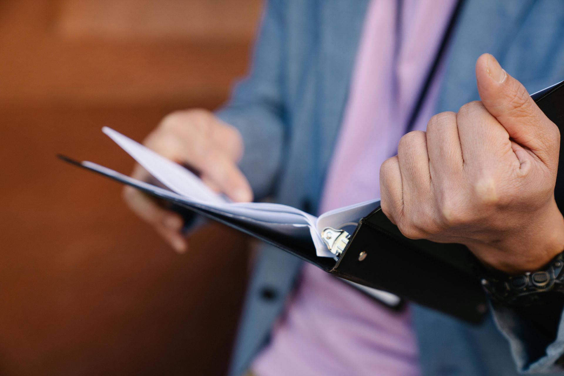 A man in a suit and tie is holding a binder with papers in it.