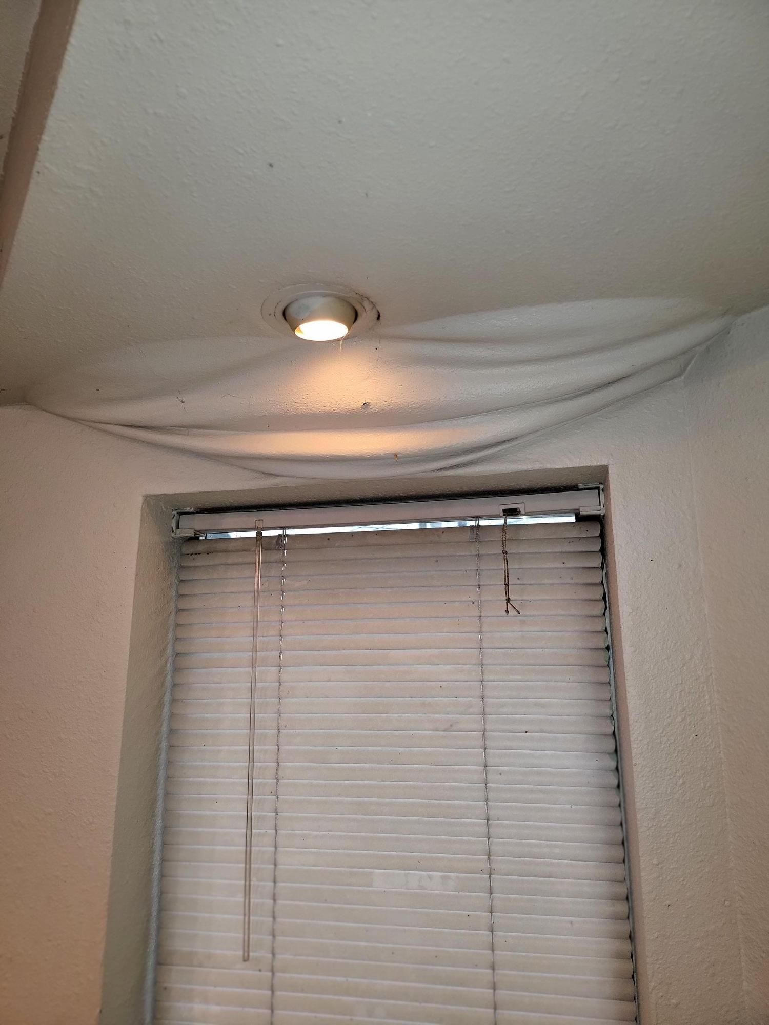 A window with blinds and a light on the ceiling.