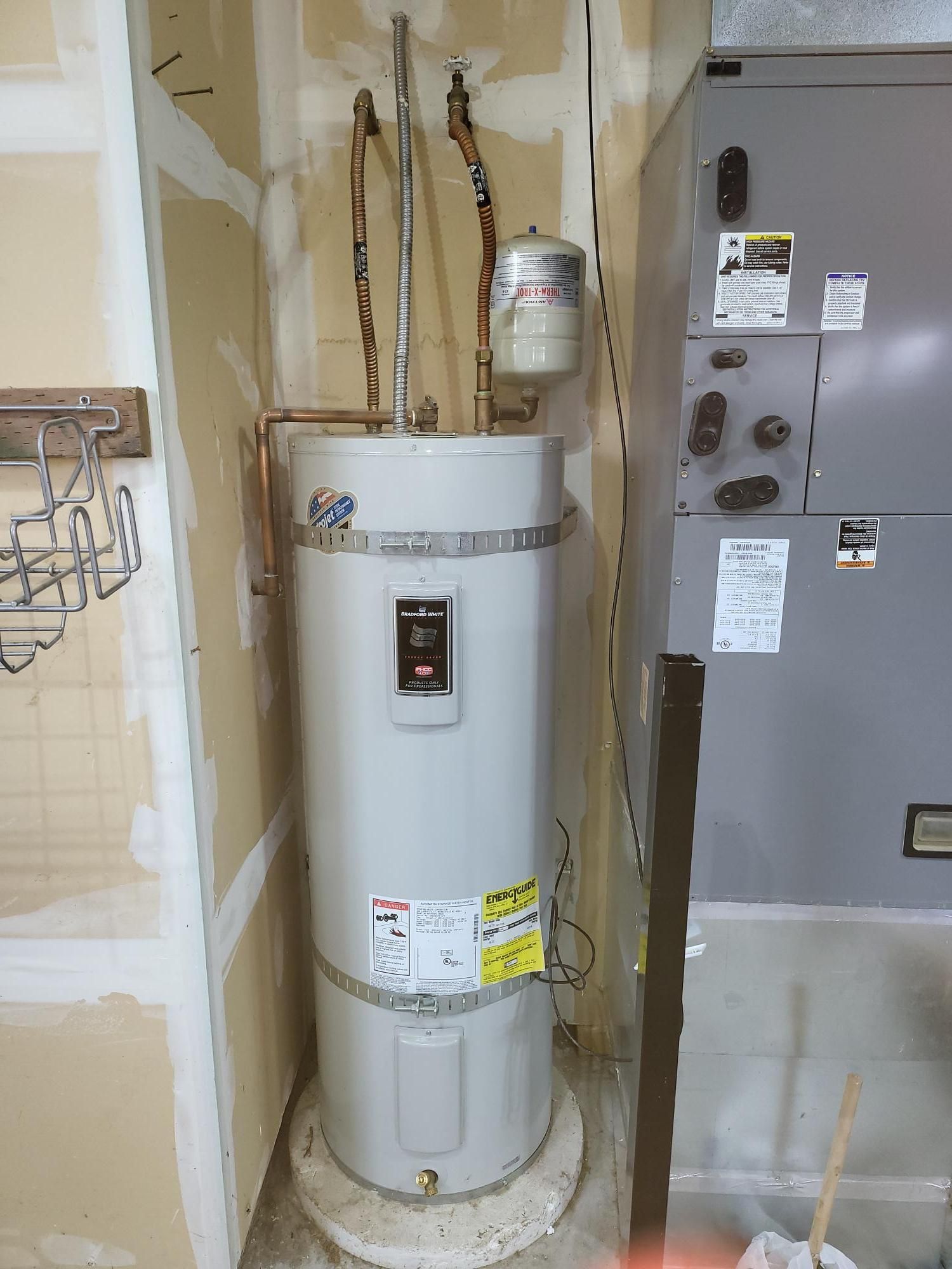 A water heater is sitting in a room next to a furnace.