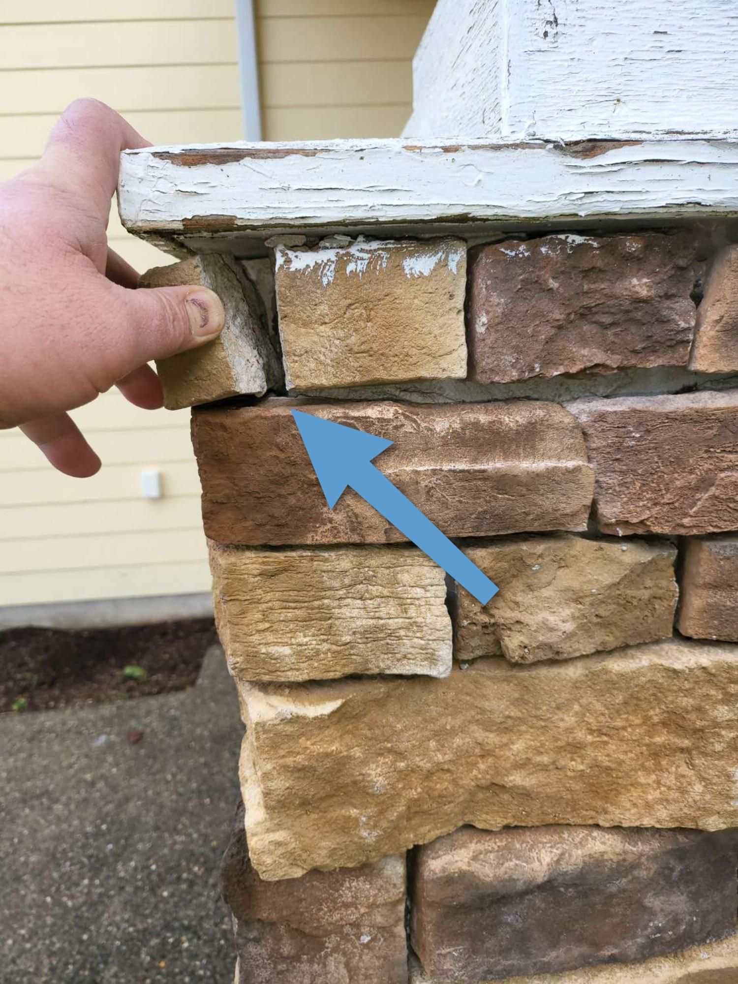 A person is holding a piece of wood over a brick wall.