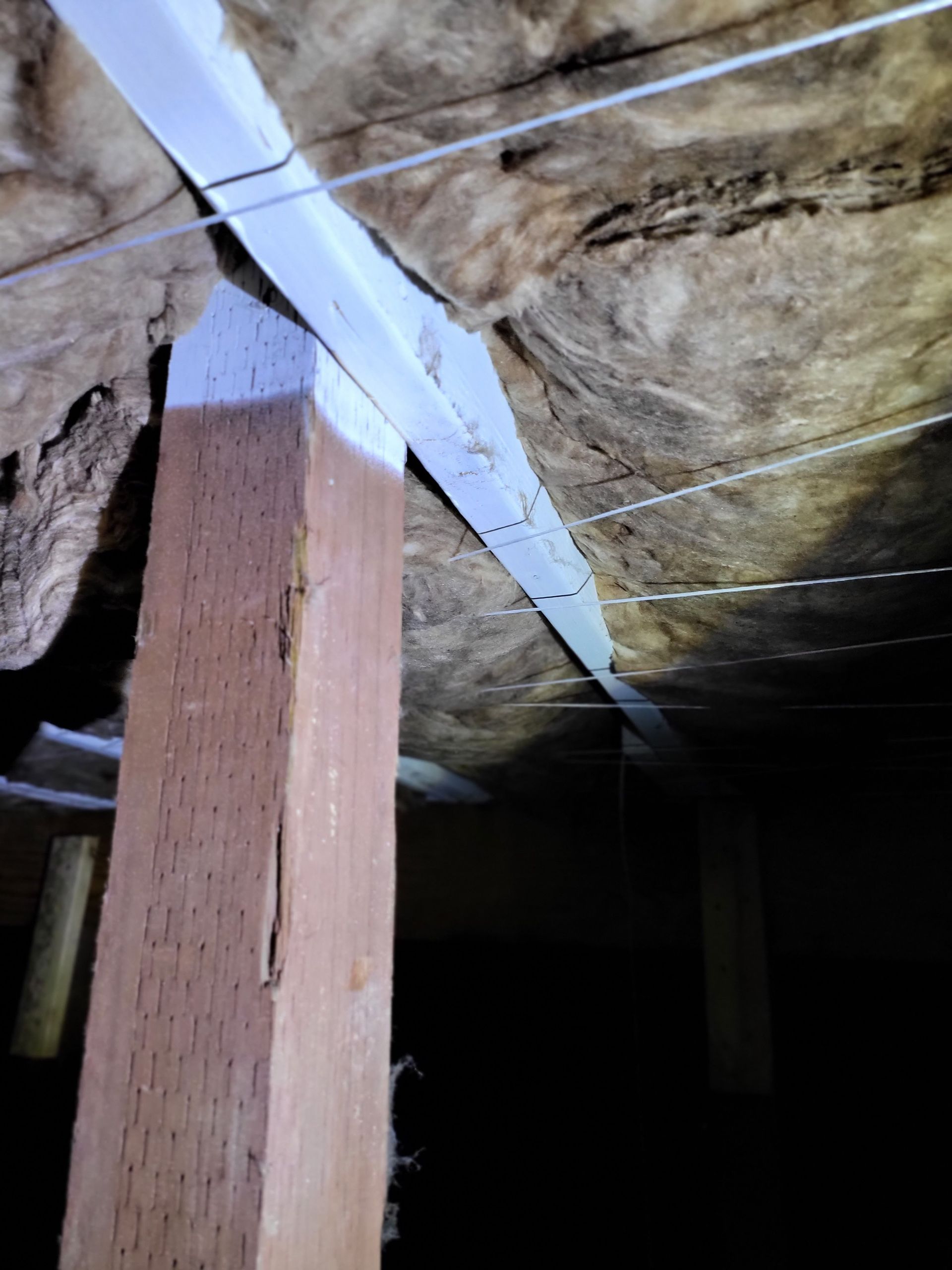A wooden post is sitting under a ceiling with insulation.